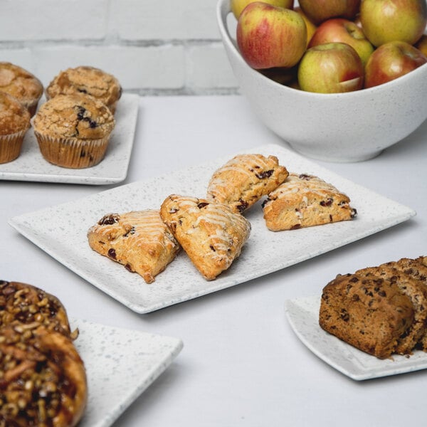 A rectangular porcelain platter with blue speckles holding pastries and apples, including a yellow apple.