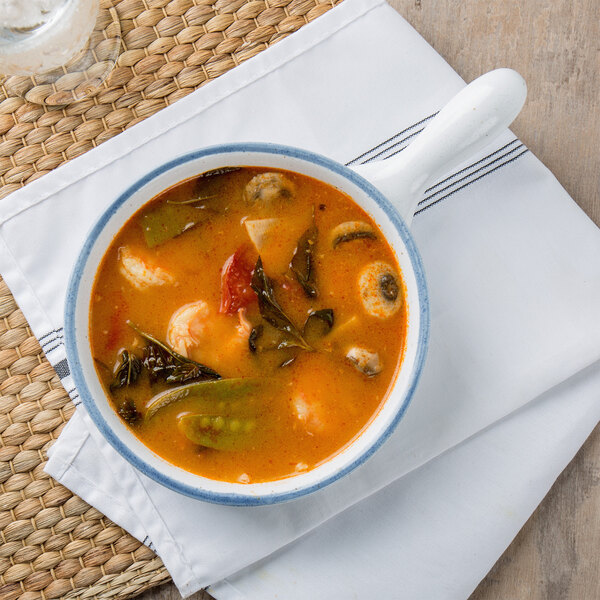 A 10 Strawberry Street Arctic Blue porcelain casserole bowl with handle filled with soup on a white plate.