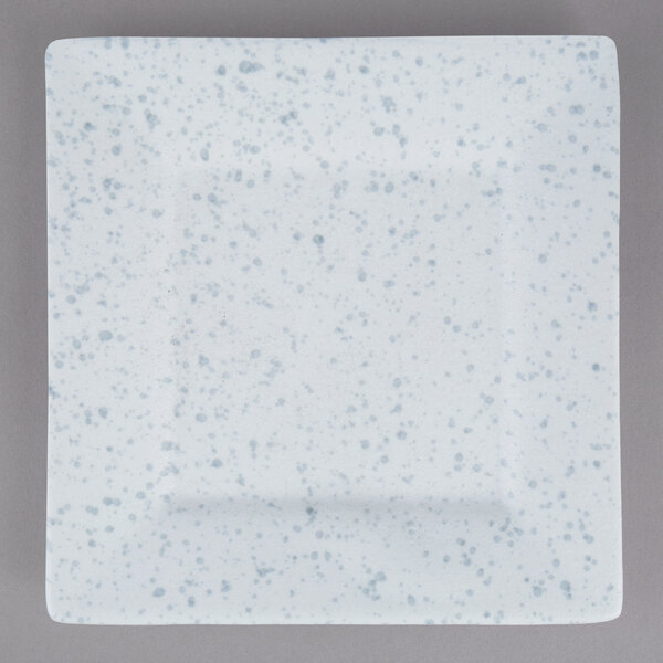 A white square porcelain dinner plate with blue speckled spots.