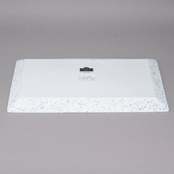 A white rectangular porcelain platter with a blue speckled design on the inside and a black label.