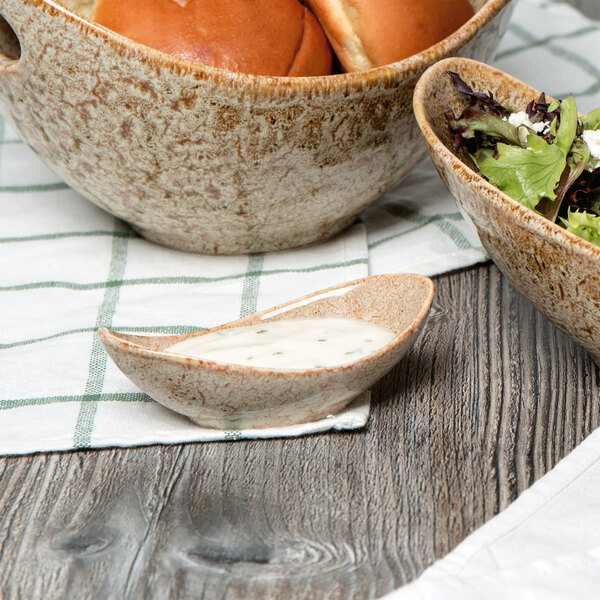 A bowl of food and a spoon with sauce in a white porcelain canoe tid bit bowl.