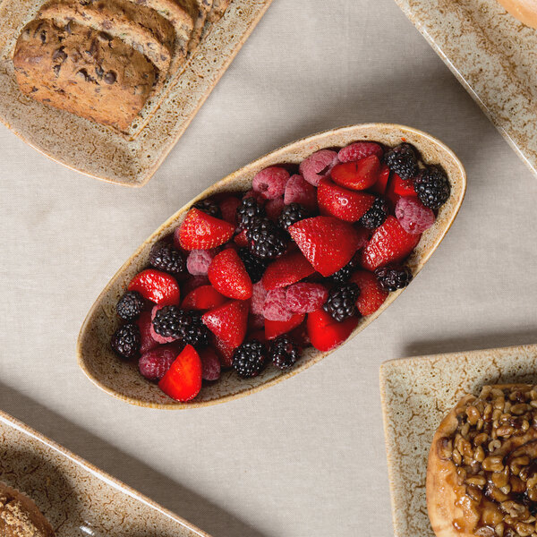 A Tiger Eye porcelain canoe bowl filled with a variety of fruit on a table.