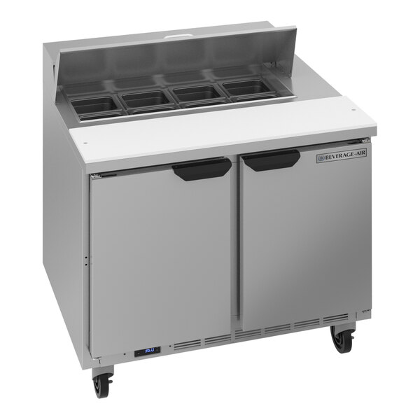 A stainless steel two-door refrigerated sandwich prep table with a raised ingredient rail and cutting board.