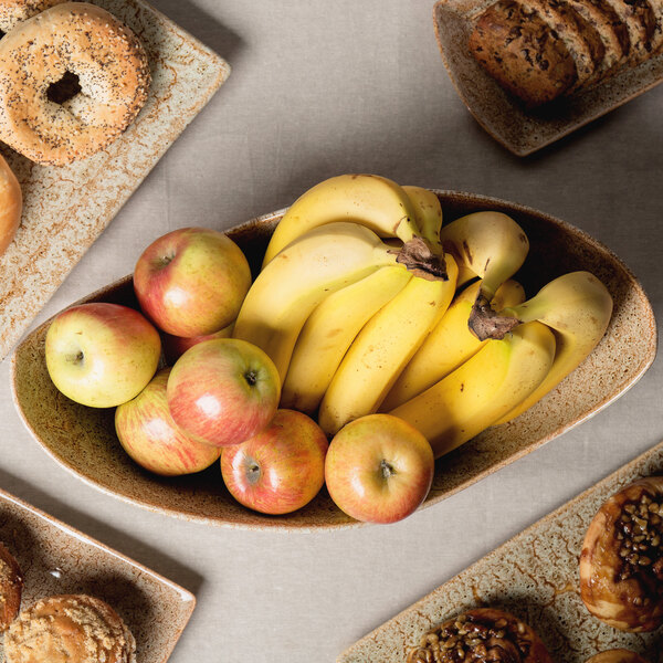 A 10 Strawberry Street Tiger Eye porcelain canoe bowl filled with bananas, red apples, and bread.