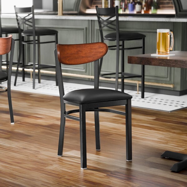 A black metal chair with a black vinyl seat and an antique walnut wood backrest.