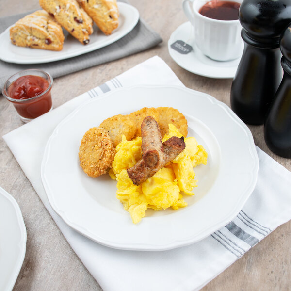 A Tuxton TuxTrendz white scalloped china plate with breakfast food on a table.