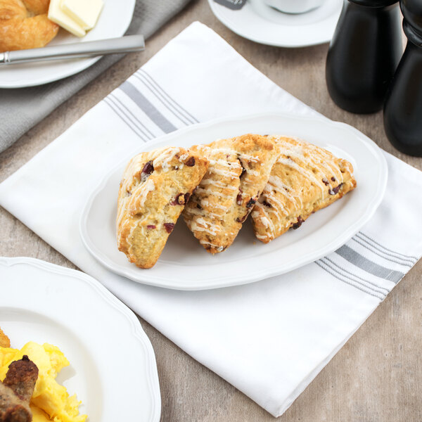 A Tuxton white china oval platter with pastries and breakfast items on it.