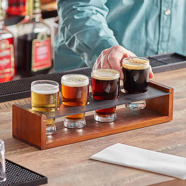 A man holding a tray of glasses with different colored drinks on a table in a bar.