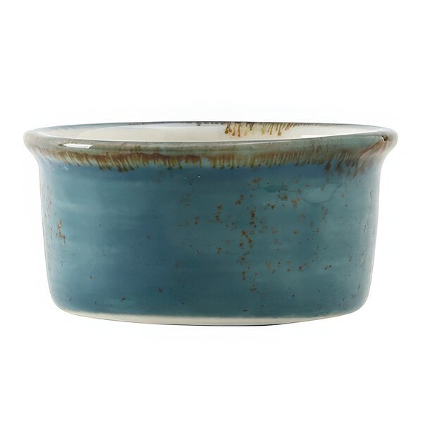 A blue ceramic Tuxton ramekin with brown specks on a table.