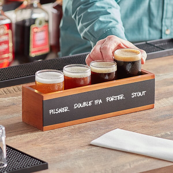 A man holding an Acopa Write-On Flight Crate with Barbary Tasting Glasses filled with beer on a table in a brewery tasting room.