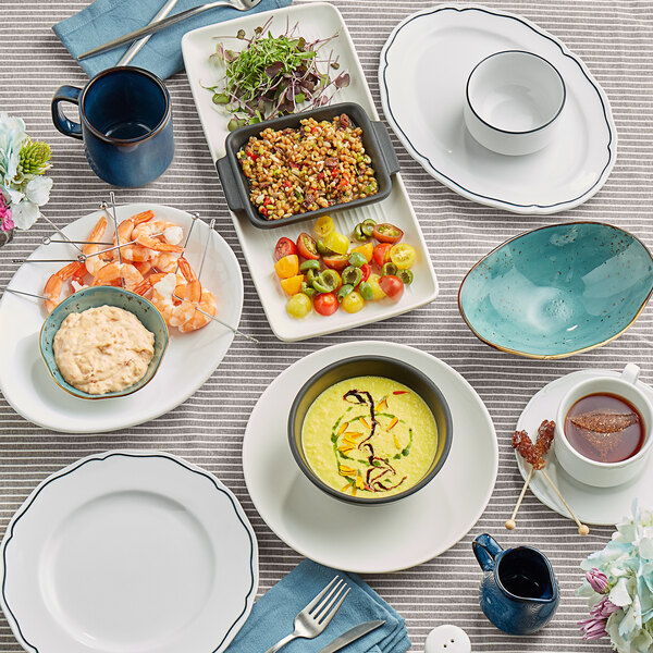 A white Tuxton china cup with a scalloped edge on a table with food