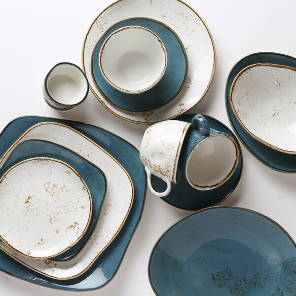 A stack of TuxTrendz Artisan Geode Azure china ellipse plates with white and brown speckled accents.