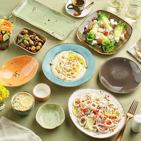 A table with Tuxton Artisan Geode Agave ellipse plates and bowls of food on it.