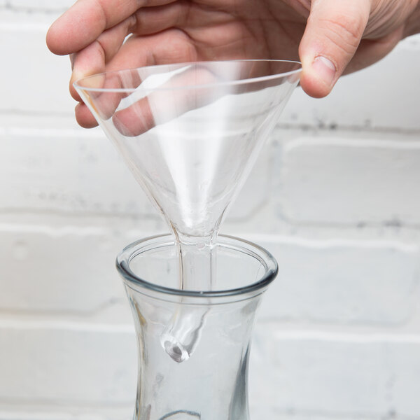 A hand using a Franmara glass decanter funnel to pour liquid into a glass.