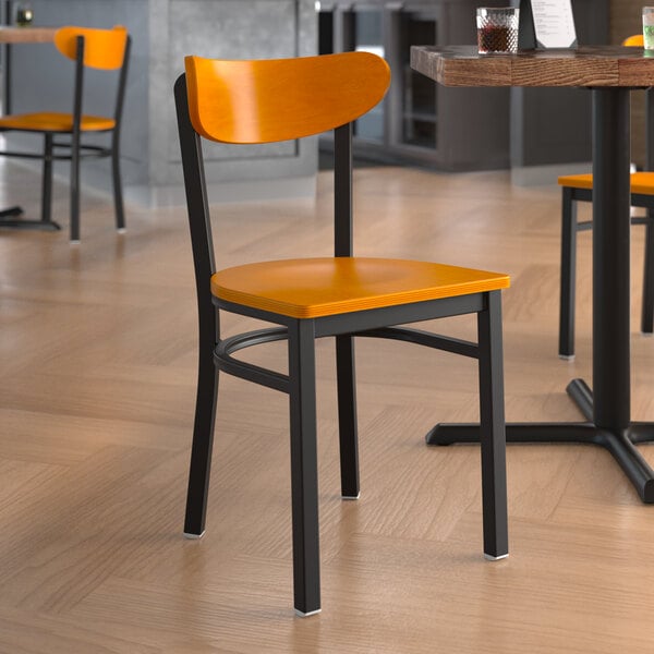 A Lancaster Table & Seating Boomerang Series black metal chair with a cherry wood seat and back on a table in a restaurant dining area.