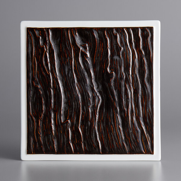 A white square china plate with black and brown designs.