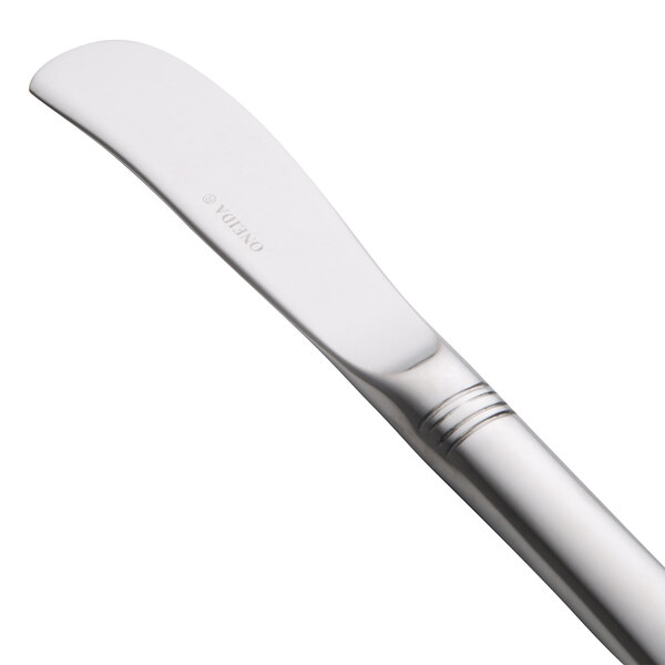 An Oneida Astragal stainless steel butter spreader with an 18/10 stainless steel finish and white handle.