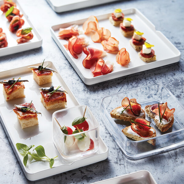 A catering table with rectangular white porcelain Arcoroc plates holding a variety of food items.