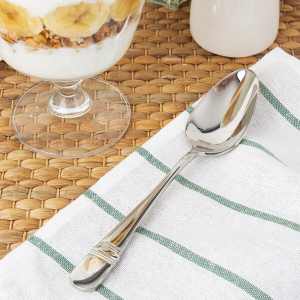 A Oneida stainless steel oval bowl spoon on a napkin next to a glass of yogurt.