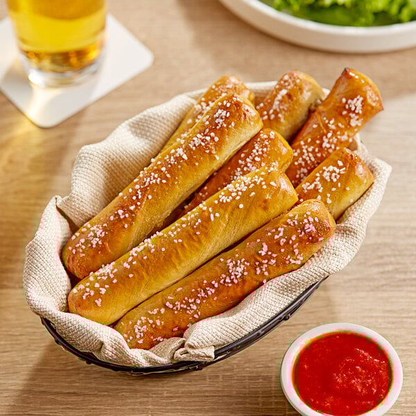 A basket of Dutch Country Foods Pennsylvania Dutch Soft Pretzel Sticks with red sauce on a table.