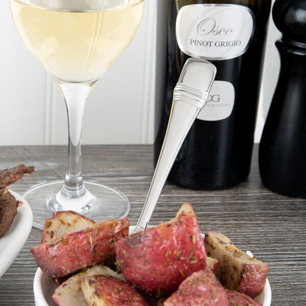 An Oneida Astragal heavy weight stainless steel serving spoon in a bowl of red potatoes on a table with a glass of white wine.