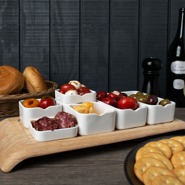 A wooden tray with a variety of food on a table with white rectangular bowls filled with food.