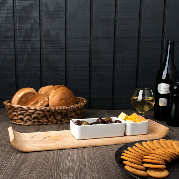 A wood board with a white rectangular Arcoroc bowl of food and a glass of yellow liquid.