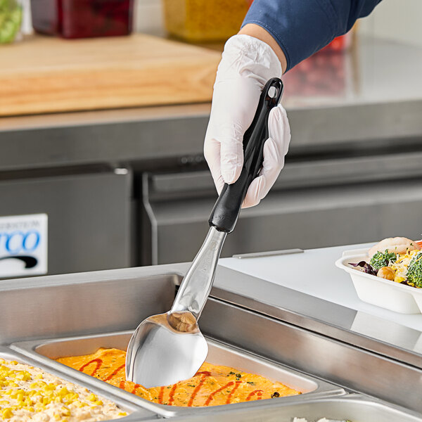 A person in gloves with a black handle using a Vollrath Jacob's Pride 3-sided solid basting spoon to serve food.