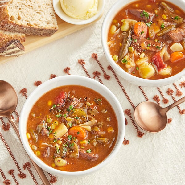 Two bowls of Spring Glen Fresh Foods vegetable soup with beef on a table with spoons and bread.