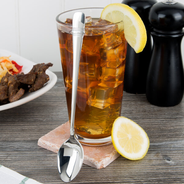 An 1880 Hospitality stainless steel iced tea spoon next to a glass of iced tea with a lemon.