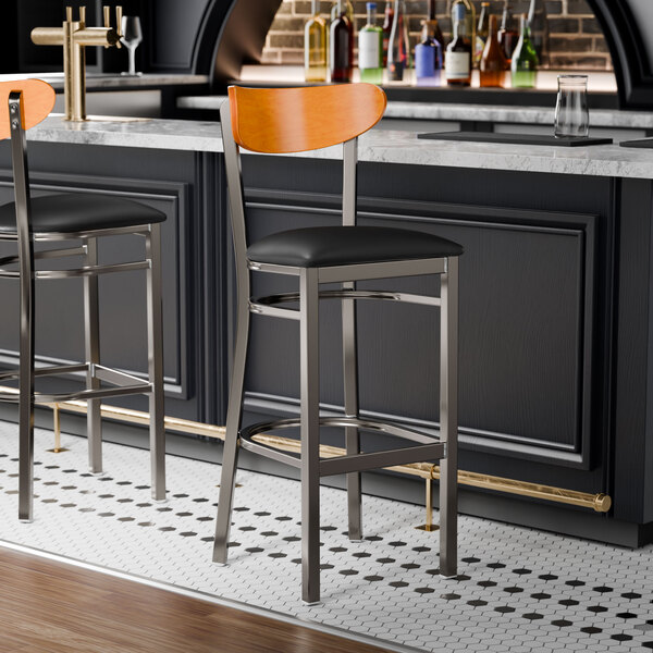 A Lancaster Table & Seating bar stool with a black cushion and cherry wood back on a counter.
