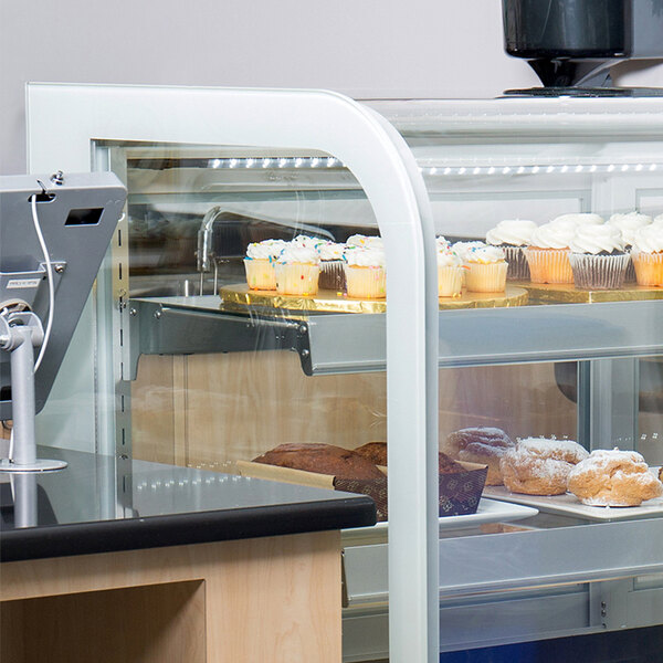 A woman standing in front of a bakery display case with cupcakes on the bottom shelf.