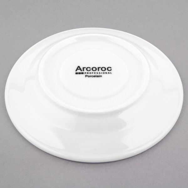 A white porcelain saucer with the word Arcoroc in black text.