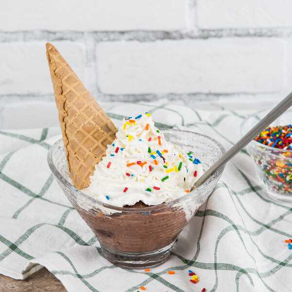 An Arcoroc Jazzed glass bowl of chocolate ice cream with sprinkles and a waffle cone.