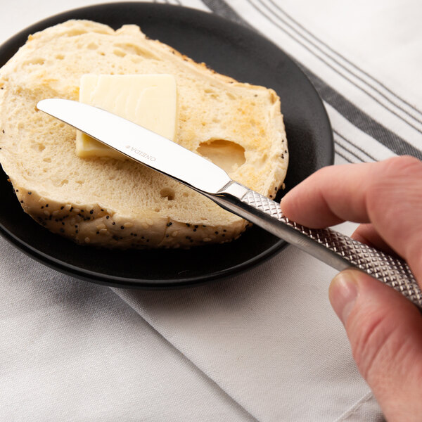 A person holding a Oneida Jade stainless steel butter knife over a piece of bread.