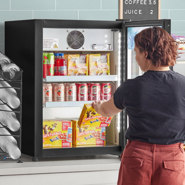 A woman opening an Avantco countertop display refrigerator filled with food.