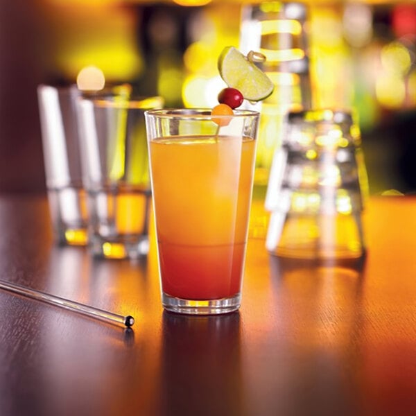 A stack of Arcoroc Stack Up Cooler Glasses with orange and yellow drinks and fruit on top on a table.