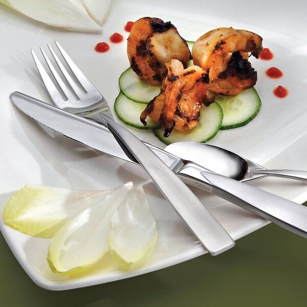 A Oneida Stiletto stainless steel steak knife on a plate with a spoon and knife.