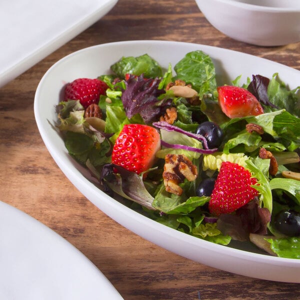 A salad in an Elite Global Solutions Tenaya off white melamine oval plate with strawberries, blueberries, and nuts.