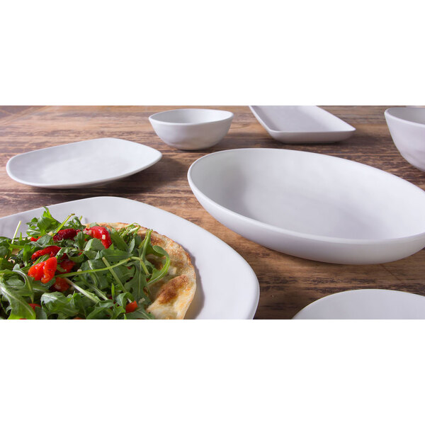 An off white Elite Global Solutions Tenaya melamine serving bowl on a wood surface with food in it.