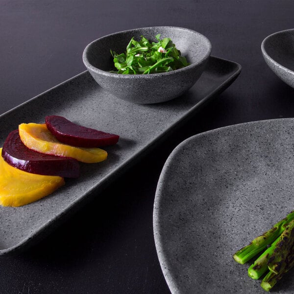 A close up of a granite stone Elite Global Solutions melamine bowl filled with green leaves and beets.