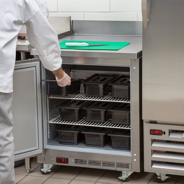 A chef in a kitchen placing black containers into a Beverage-Air worktop freezer.