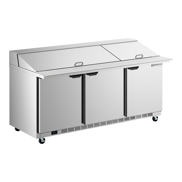 A stainless steel, three-door mega top ADA height refrigerated sandwich prep table with a flat top and casters.