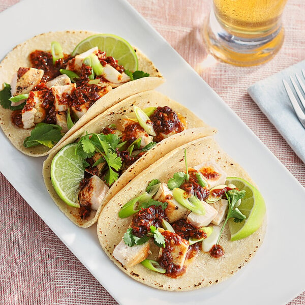 A plate of tacos with Chipotle Peppers in Adobo sauce, limes, and a glass of beer.