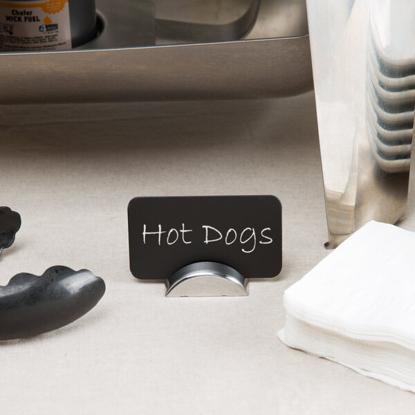 A stainless steel semicircle table card holder with a black label on a table counter next to napkins and a sausage.