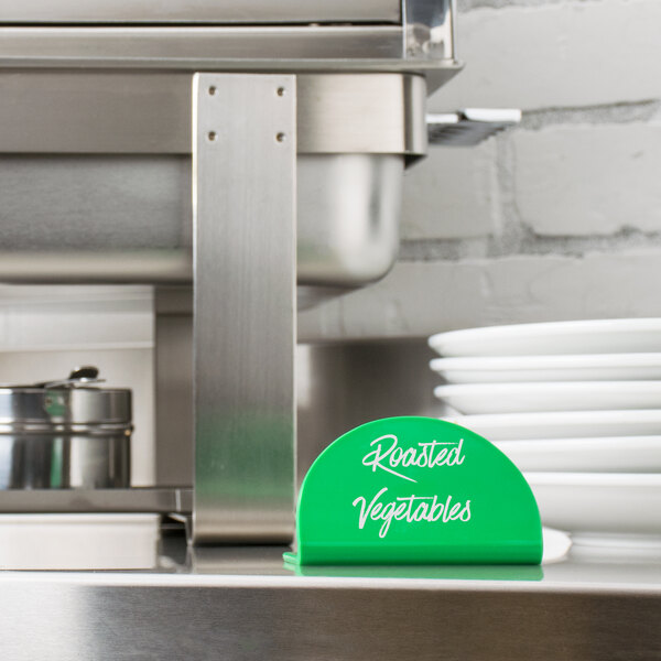 A green Tablecraft melamine table tent on a counter with a sign that says roasted vegetables.