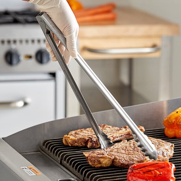 A person using Edlund heavy-duty scallop tongs to turn meat on a grill.