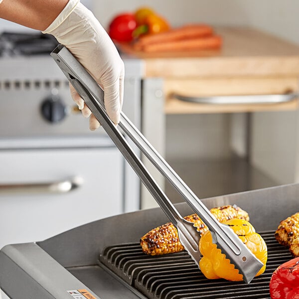 A person using Edlund heavy-duty gripper tongs to grill corn on the cob.