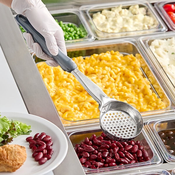 A person in gloves using a Vollrath grey perforated round Spoodle to serve beans over a plate of salad.