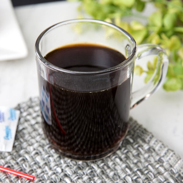 A stackable Arcoroc tempered glass mug filled with coffee on a white background.